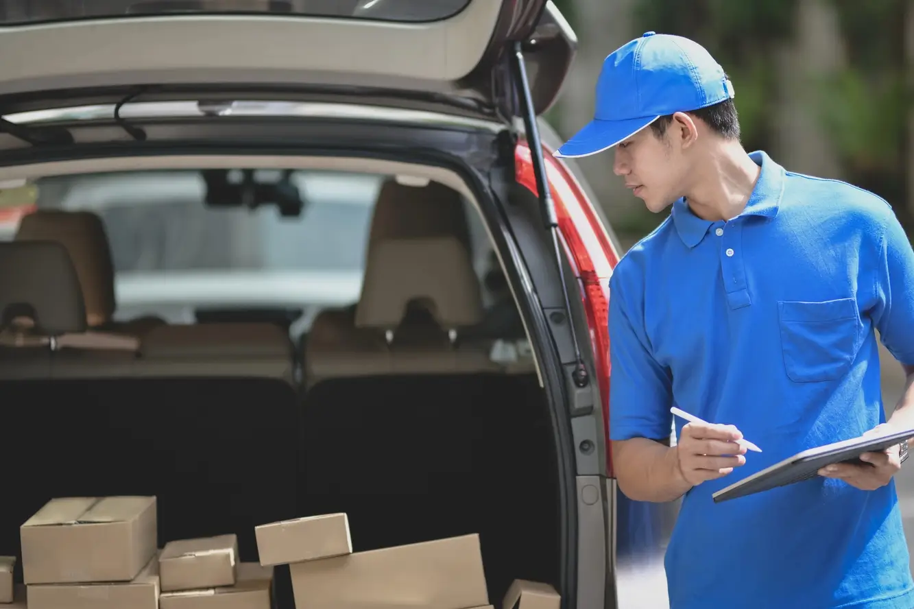 A delivery driver in a blue shirt and hat stands at the back of his vehicle while performing Colorado transportation delivery services on the Front Range.