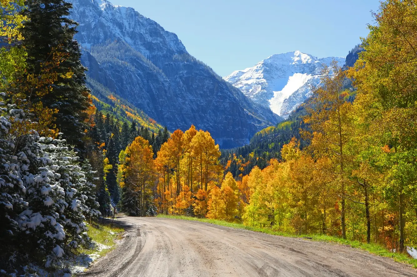 Colorado mountain scenery in autum with newly fallen snow in the background mountains with a dirt road in the foreground showing Cirrus Transportation service areas in Colorado.